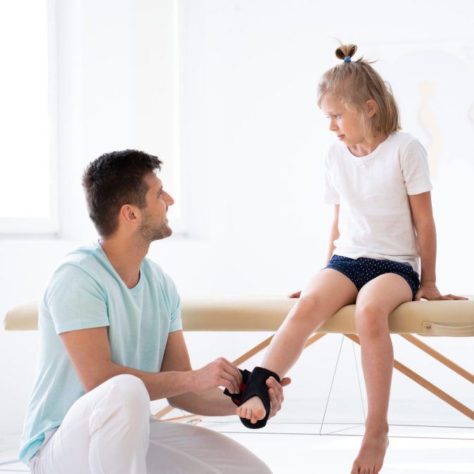Cute little injure girl on massage table exercising with young male doctor Cute little injure girl on massage table exercising with young male doctor